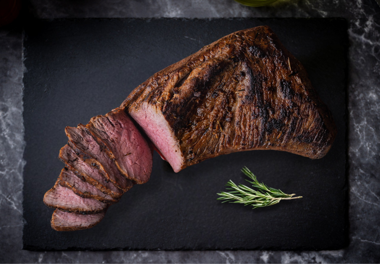 Cooked Sirloin Tri-Tip. sliced steak on a dark slate surface with rosemary