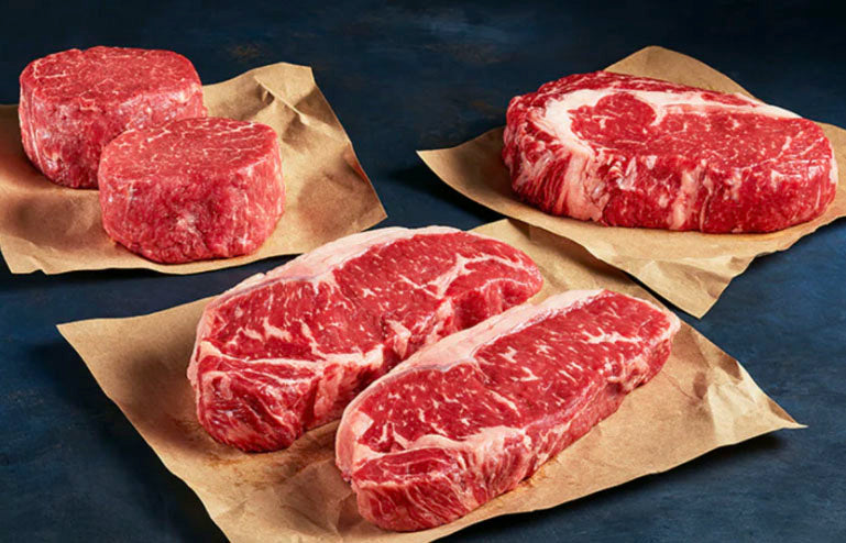 Raw red meat steaks on brown paper with a dark background