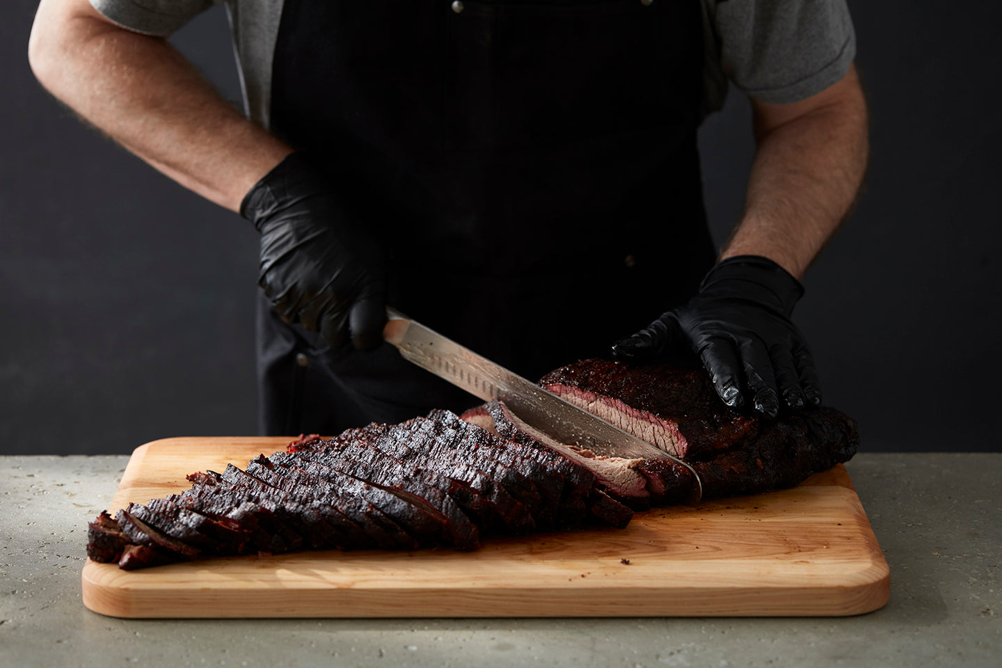 Gloved man slicing brisket on a cutting board