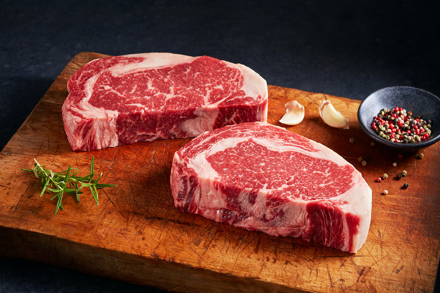 Two Raw Ribeye Steaks on a Butcher Board