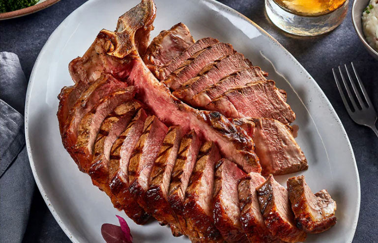 Sliced ribeye steak on a white plate with a glass of beer in the background