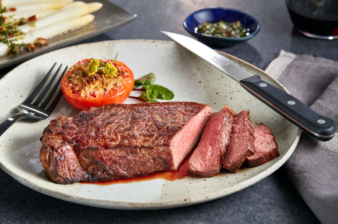 Cooked striploin steak sliced on a place with a tomato.