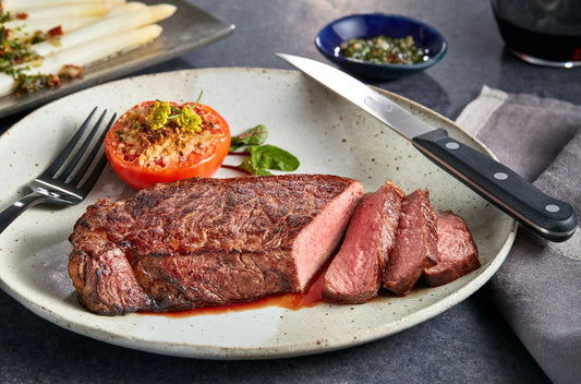 Cooked striploin steak sliced on a place with a tomato.