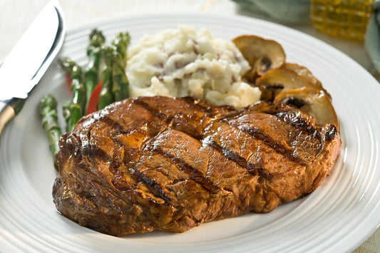 Cooked ribeye on a plate with mushrooms, mashed potatoes and asparagus.